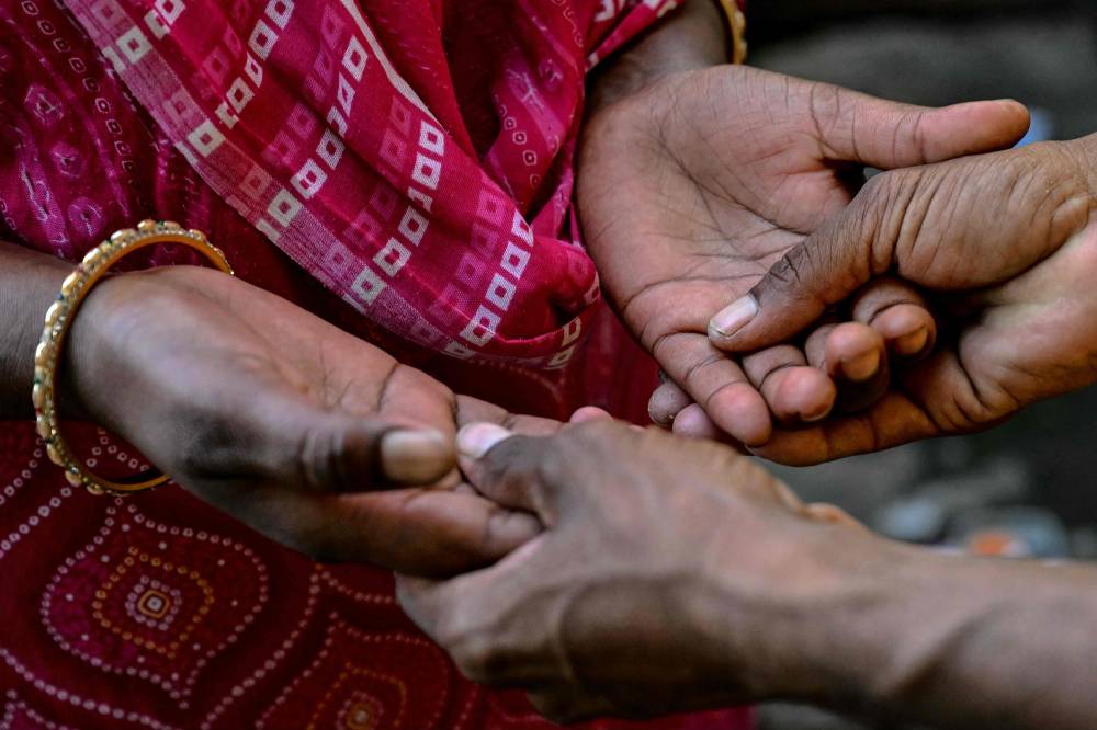 In this photograph taken on May 4, 2025, Jyoti Thorat (L), a sugarcane worker who was married as a child bride, holds her husband Ravindra's hands as they talk near their home at Kathoda village in Beed district of India's state of Maharashtra. - (Photo by INDRANIL MUKHERJEE / AFP)