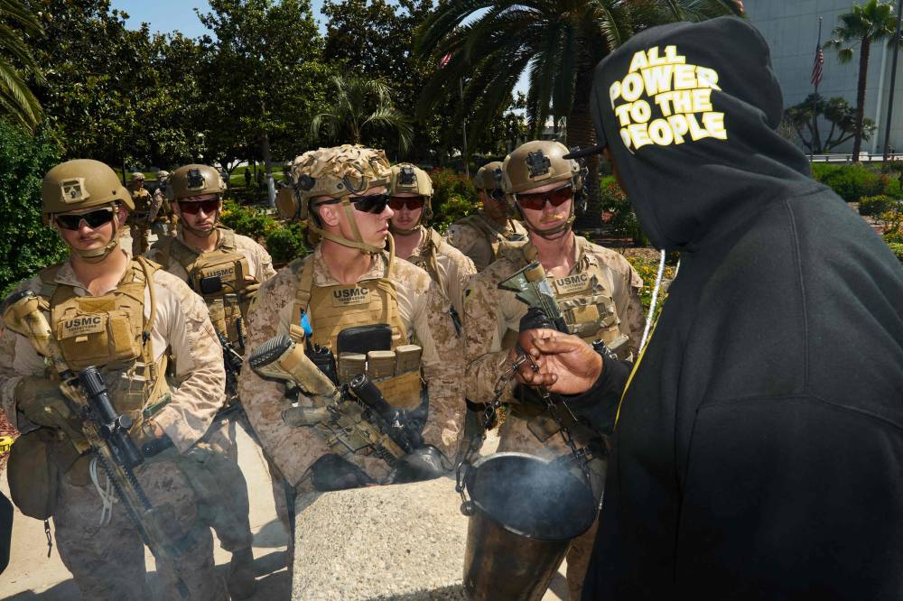 A demonstrator burning sage speaks to US Marines from 2nd Battalion, 7th Marines, standing guard at a protest condemning the US and Israeli strikes on Iran, outside the Westwood Federal Building in the Westwood neighbourhood of Los Angeles, on June 22, 2025. (Photo by Bing Guan / AFP)