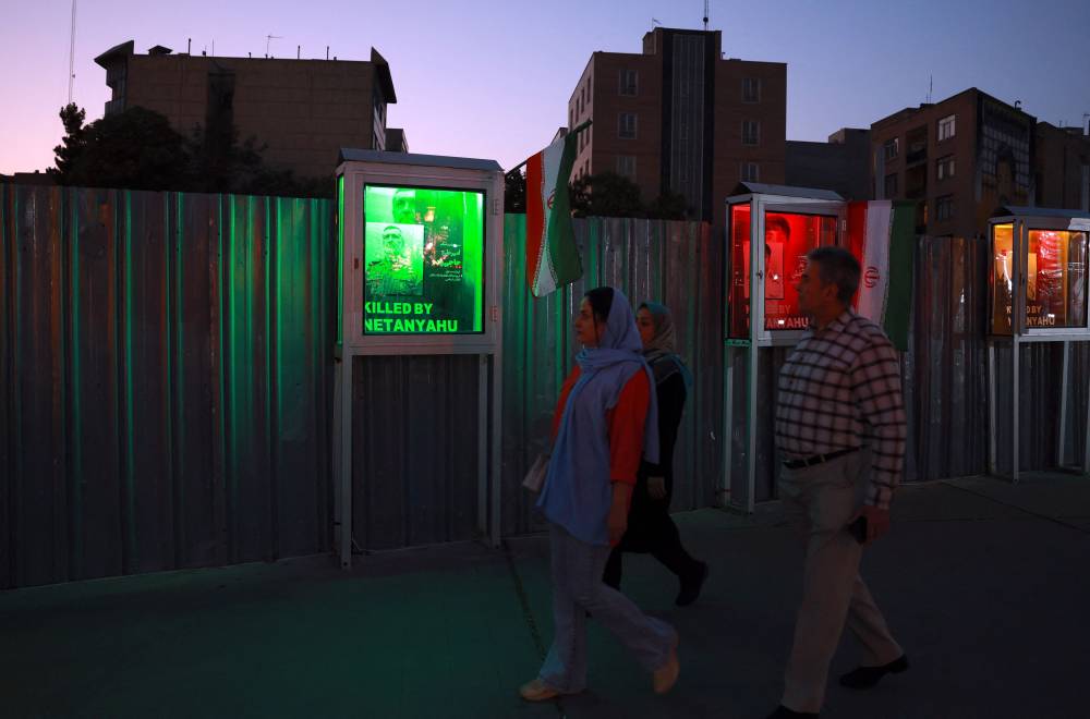 Iranians walk past next to an image of the late commander of the IRGC Aerospace Forces Amir Ali Hajizadeh, with the slogan 'Killed by Natanyahu' at a memorial for those killed by Israel, at Hafteh-tir Square, in Tehran on June 23, 2025. United Nations investigators warned on June 23, of the 