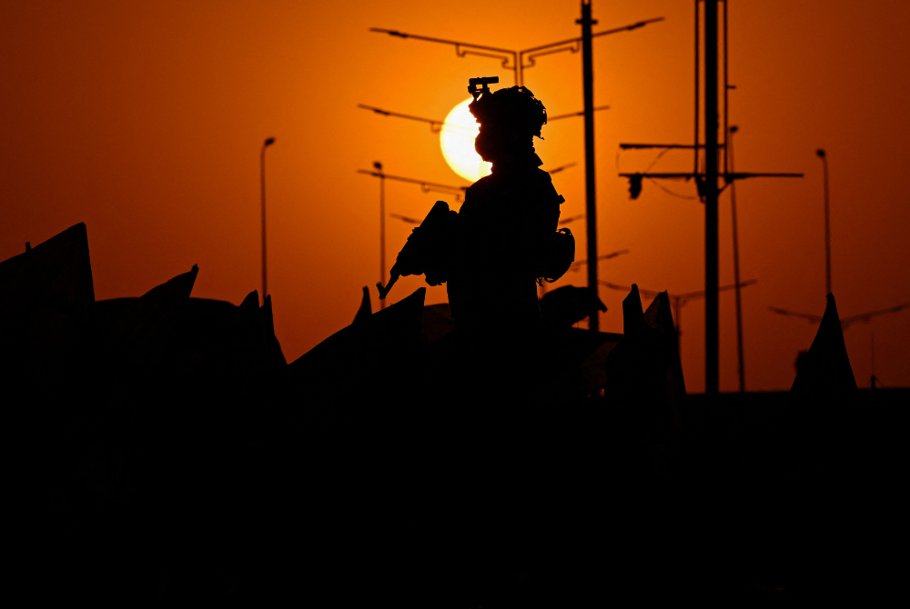 An Iraqi soldier stands guard as people march during celebrations to mark the ceasefire between Israel and Iran in the southern Iraqi city of Basra on June 24, 2025. (Photo by Hussein FALEH / AFP)