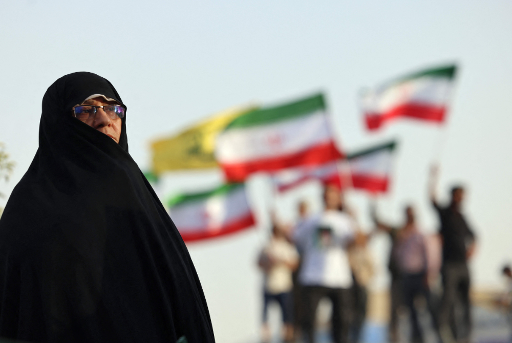 An Iranian woman looks on as people wave national flags as they celebrate a ceasefire between Iran and Israel at Enghlab Square in the capital Tehran on June 24, 2025. (Photo by ATTA KENARE / AFP)