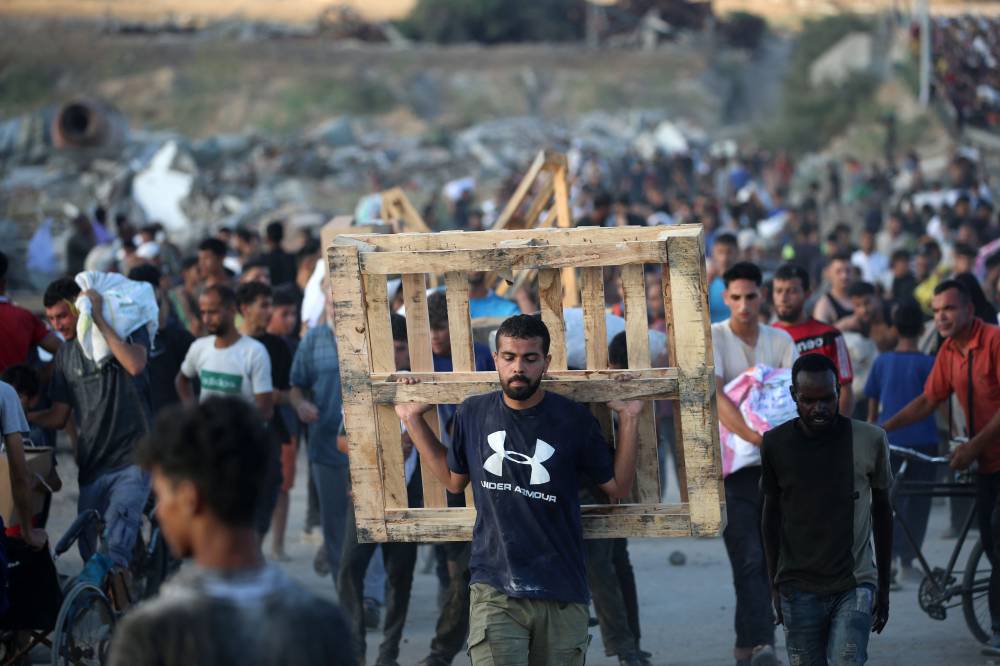 A man carrying a wooden pallet, walks along the Salah al-Din road near the Nusseirat refugee camp in the northern Gaza Strip, used by food-seeking Palestinians to reach an aid distributution point set up by the privately-run Gaza Humanitarian Foundation (GHF), on June 25, 2025. (Photo by Eyad BABA / AFP)