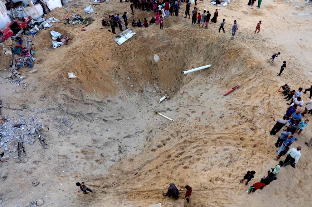 Palestinians gather around a huge crater after the Israeli army targeted the tents of displaced people in the northern Al-Rimal neighborhood of Gaza City on June 28, 2025. (Photo by Omar AL-QATTAA / AFP)