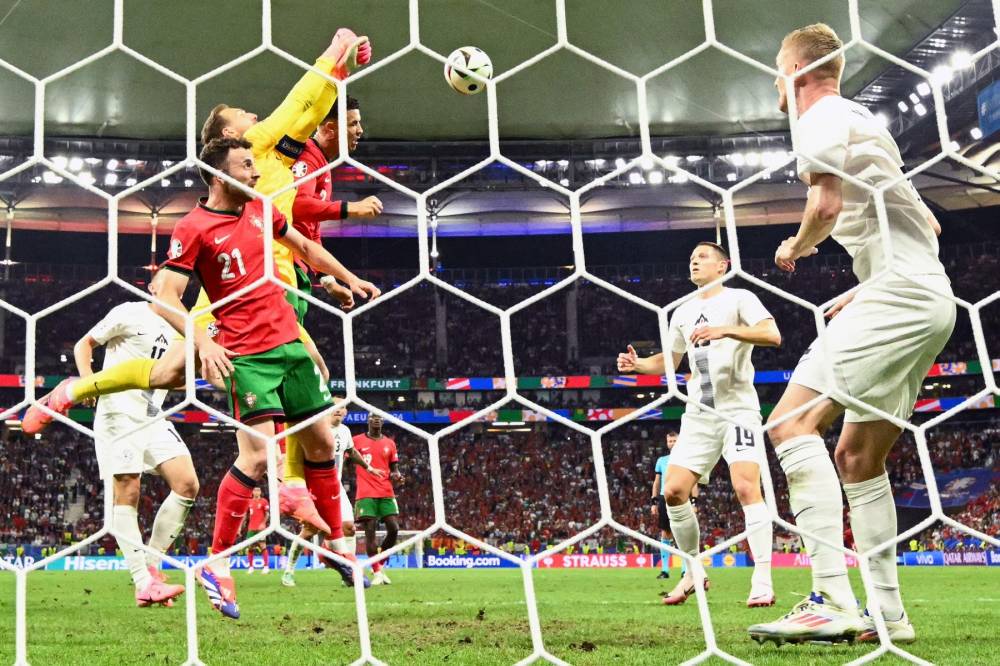 Slovenia's goalkeeper #01 Jan Oblak jumps to punch the ball clear next to Portugal's forward #07 Cristiano Ronaldo and Portugal's forward #21 Diogo Jota during the UEFA Euro 2024. Photo by Angelos Tzortzinis/AFP FILE PIX