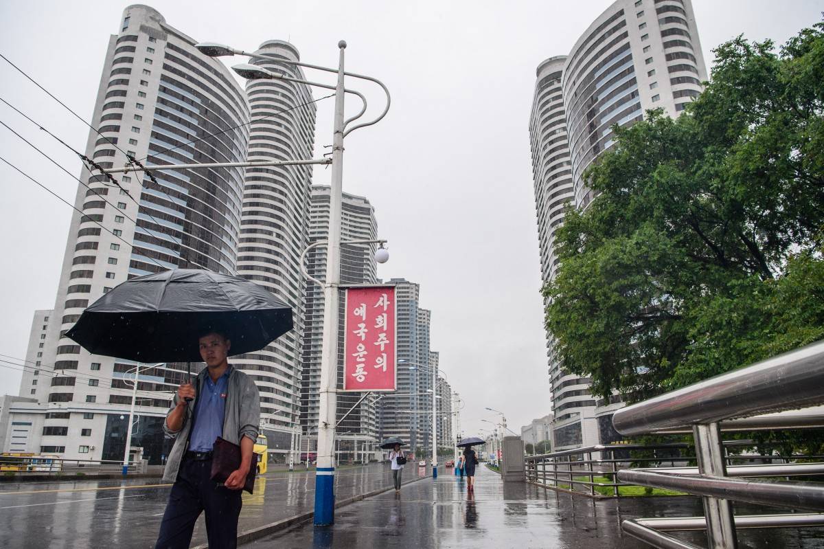 People use umbrellas to shelter from heavy rain as they walk along Changjon Street in Pyongyang on June 20, 2025. (Photo by KIM Won Jin / AFP)
