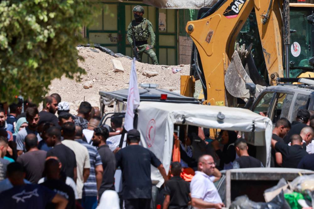 An Israeli soldier keeps watch as Palestinian residents wait at the entrance of Tulkarem camp, in the occupied West Bank, during a military operation on July 6, 2025. Photo by Jaafar Ashtiyeh/AFP