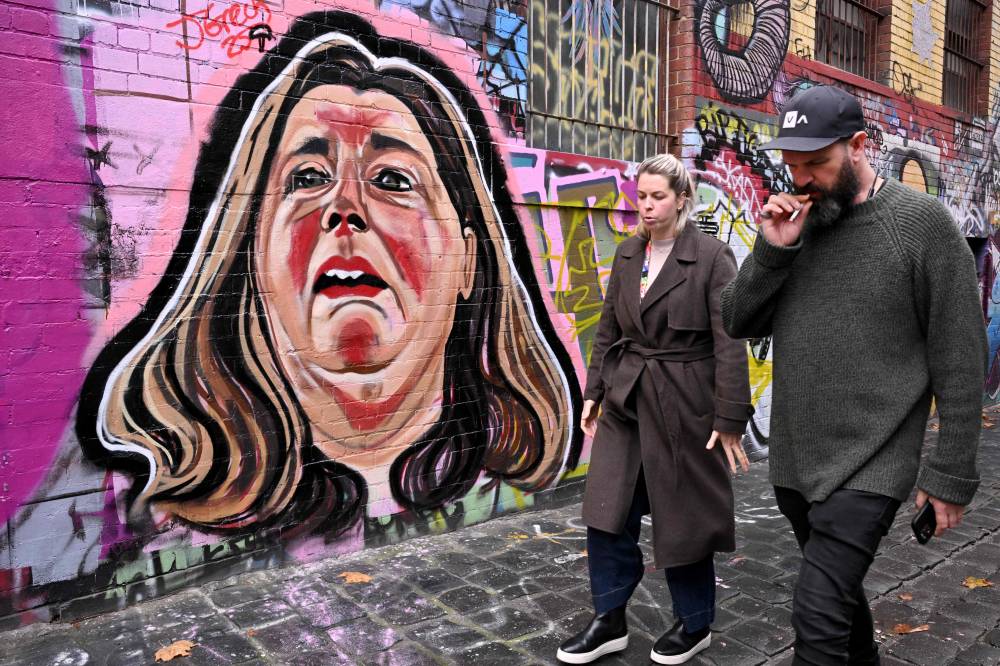This photo taken on June 17, 2025 shows people in a Melbourne laneway walking past a mural by street artist Jarrod Grech of Erin Patterson, an Australian woman accused of murdering three members of her husband's family with a toxic mushroom-laced beef Wellington lunch. - (Photo by WILLIAM WEST / AFP)