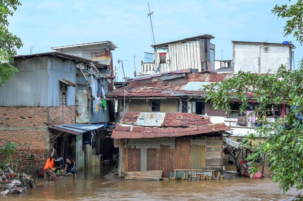 People try to save their belongings from floodwaters that inundated their neighbourhood following heavy rainfall in Jakarta on July 7, 2025. (Photo by BAY ISMOYO / AFP)