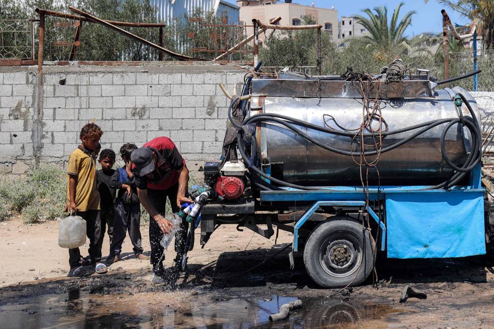 A man draws water into a bottle from the tank of a destroyed mobile water cistern that was hit by Israeli bombardment in the Nuseirat camp for Palestinian refugees in the central Gaza Strip on July 14, 2025. (Photo by Eyad BABA / AFP)