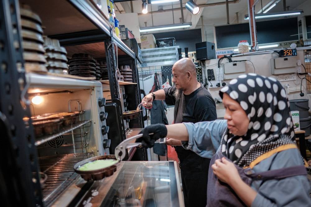 Kuih Bakar Mahanoum trader, Shahrilnizam Mohamed, 54, and his wife, Mahanum Abdul Rahman, 52, preparing their kuih bakar for sale at Larkin Sentral. Photo by Bernama