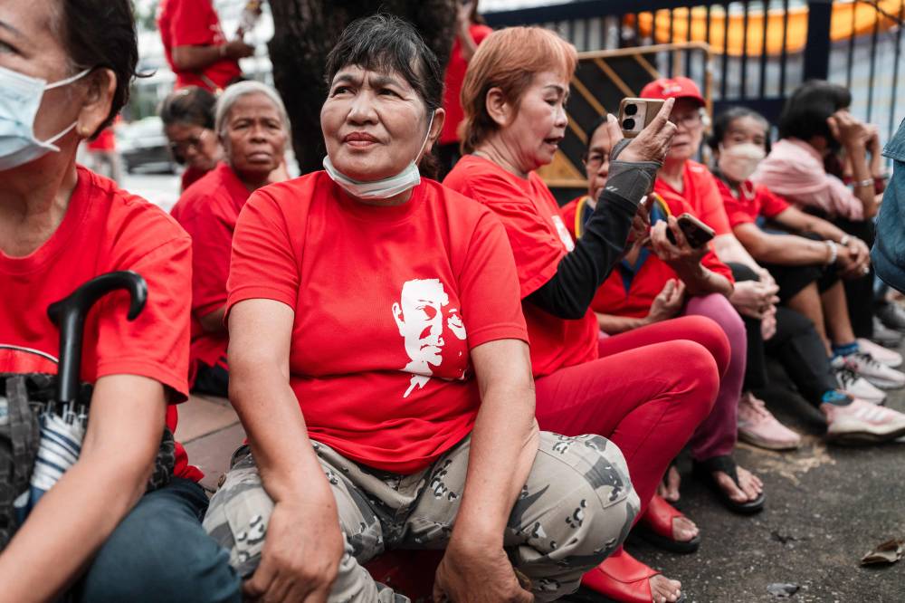 Supporters of Thailand's former prime minister Thaksin Shinawatra sit in front of the Criminal Court in Bangkok on July 16, 2025. - (Photo by Chanakarn Laosarakham / AFP)