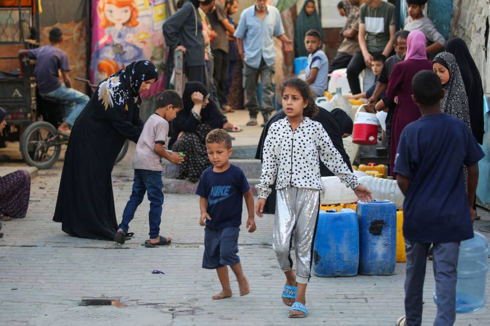 Palestinians queue near their containers as they await a water distribution truck at a makeshift displacement tent camp which was hit in Israeli strikes a day earlier, at the UNRWA-run Abou Helou school for girls at the Bureij refugee camp in the central Gaza Strip on July 17, 2025. (Photo by Eyad BABA / AFP)