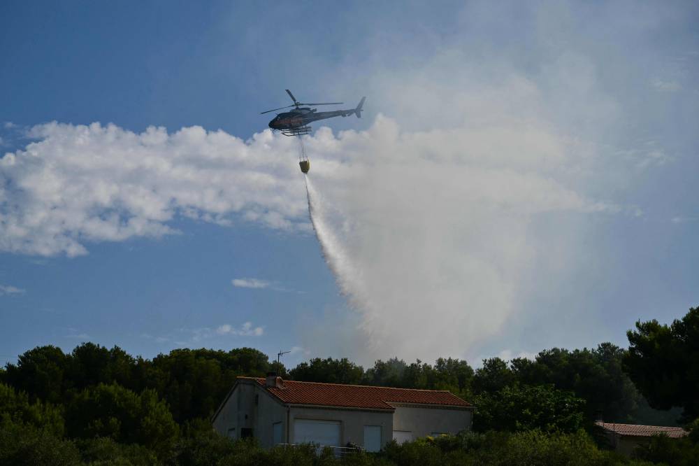 An Airbus H125 helicopter drops water over a wildfire in Saint-Julien Les Martigues, northwest of Marseille in southern France on July 18, 2025. - (Photo by CHRISTOPHE SIMON / AFP)