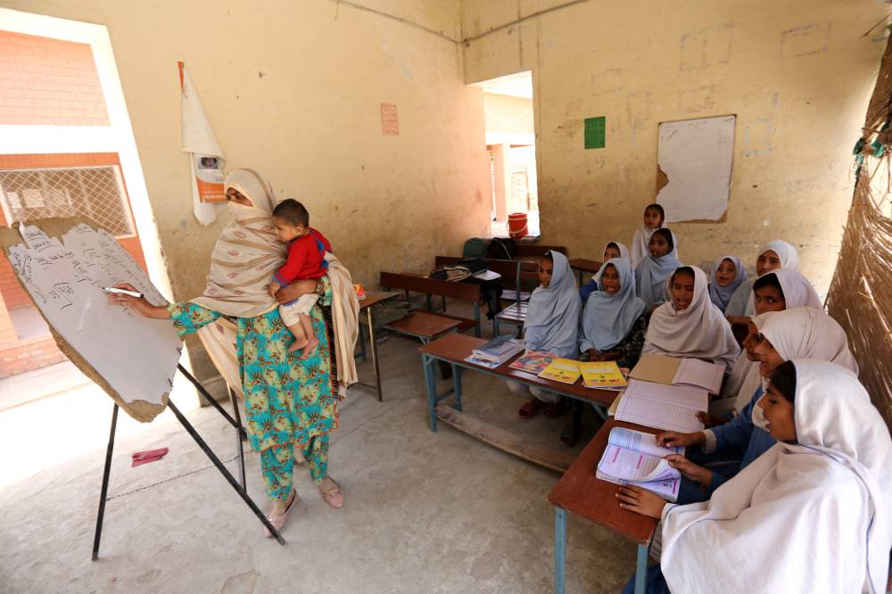 In this photograph taken on May 15, 2025, teacher Nazia Hussain (L) holds her child whilst teaching a class at a government school at Rajanpur district in southwestern Punjab province. - (Photo by Shahid Saeed Mirza / AFP)
