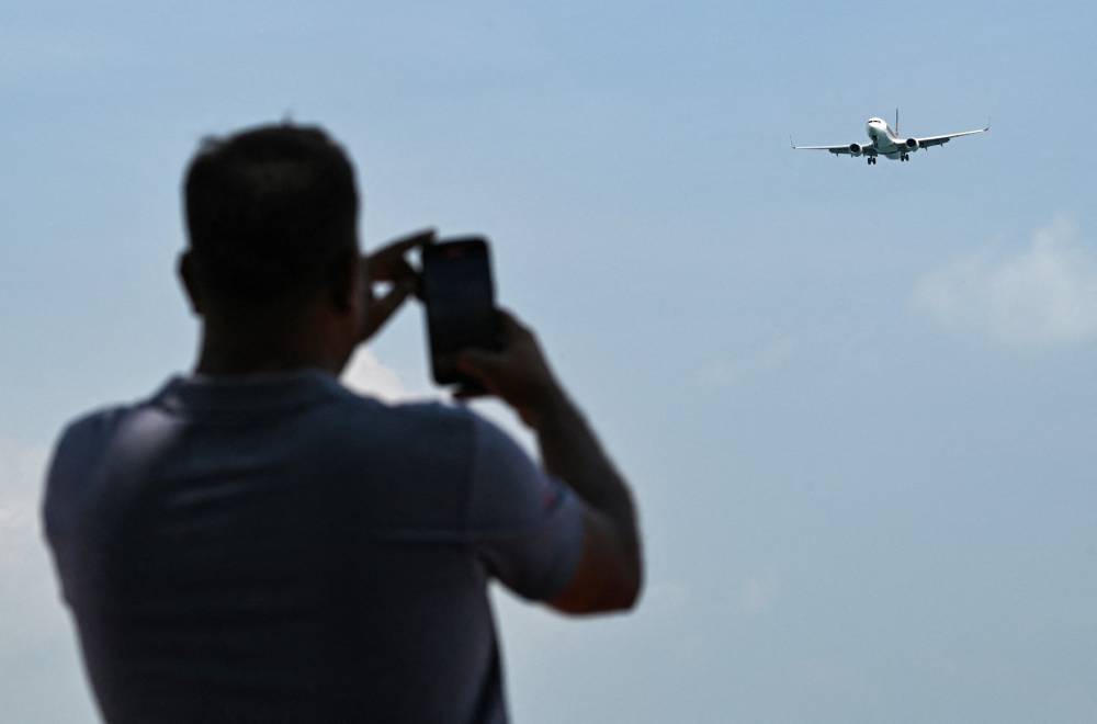 A man takes picture of a Singapore Airlines Boeing 737 approaching for landing at Singapore Changi airport in Singapore on November 5, 2024. (Photo by Roslan RAHMAN and ROSLAN RAHMAN / AFP)