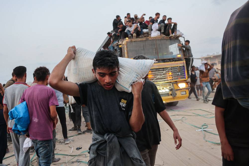 Palestinians bring back aid parcels they managed to procure as they walk on a coastal path west of Beit Lahia on July 29, 2025, after aid trucks entered the Israel-besieged Gaza Strip from the northern Zikim border crossing. (Photo by Omar AL-QATTAA / AFP)
