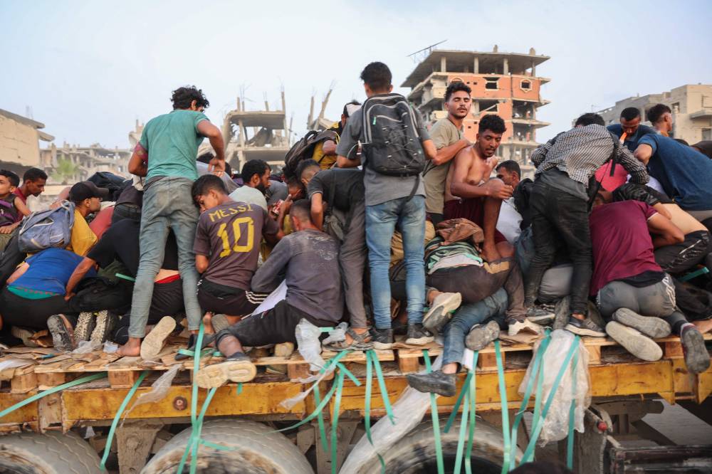 Palestinians climb in the back of a truck ona coastal path west of Beit Lahia, after managing to get aid [arcels on July 29, 2025, after aid trucks entered the Israel-besieged Gaza Strip from the northern Zikim border crossing. (Photo by Omar AL-QATTAA / AFP)
