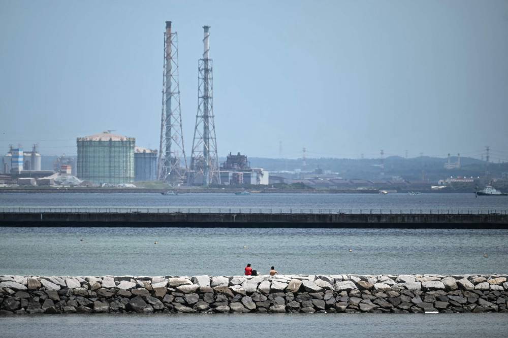 Two people (C) sit out on a breakwater after much of coastal Japan went on tsunami alert following a 8.7 magnitude quake in the sea off eastern Russia, along Tokyo Bay in Chiba City, Chiba prefecture on July 30, 2025. A powerful 8.7 magnitude earthquake off Russia's far east has prompted tsunami alerts across parts of the Pacific including Japan, Hawaii, Russia and Ecuador, and warnings along the California coast, US authorities said. - (Photo by PHILIP FONG / AFP)
