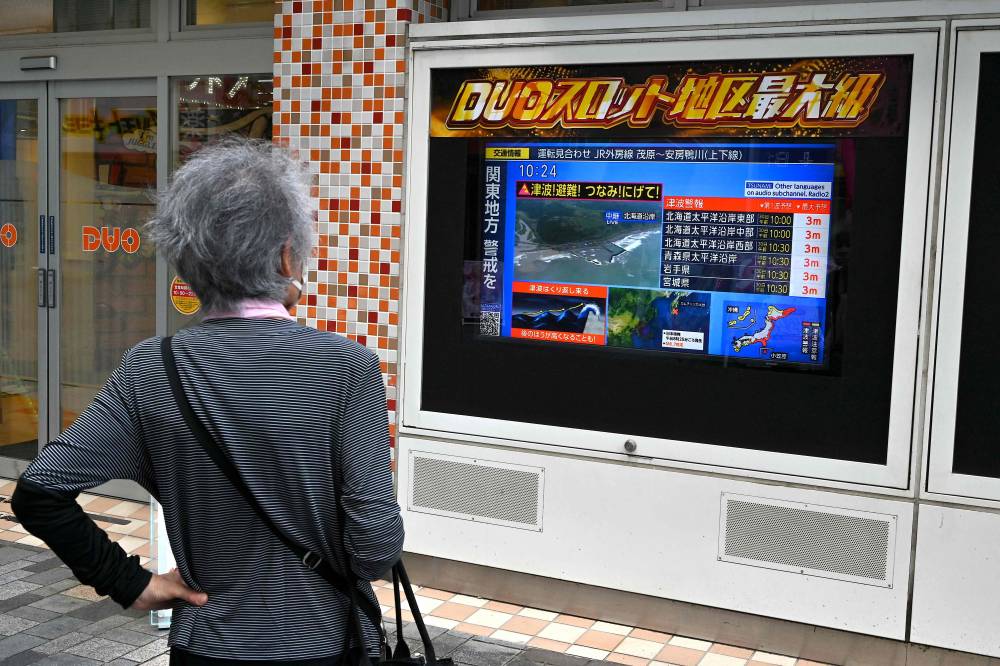 A woman watches a television broadcast of a tsunami warning for much of coastal Japan following a 8.7 magnitude quake in the sea off eastern Russia, outside a gaming shop in central Tokyo on July 30, 2025. A powerful 8.7 magnitude earthquake off Russia's far east has prompted tsunami alerts across parts of the Pacific including Japan, Hawaii, Russia and Ecuador, and warnings along the California coast, US authorities said. (Photo by Richard BROOKS and Richard A. BROOKS / AFP)