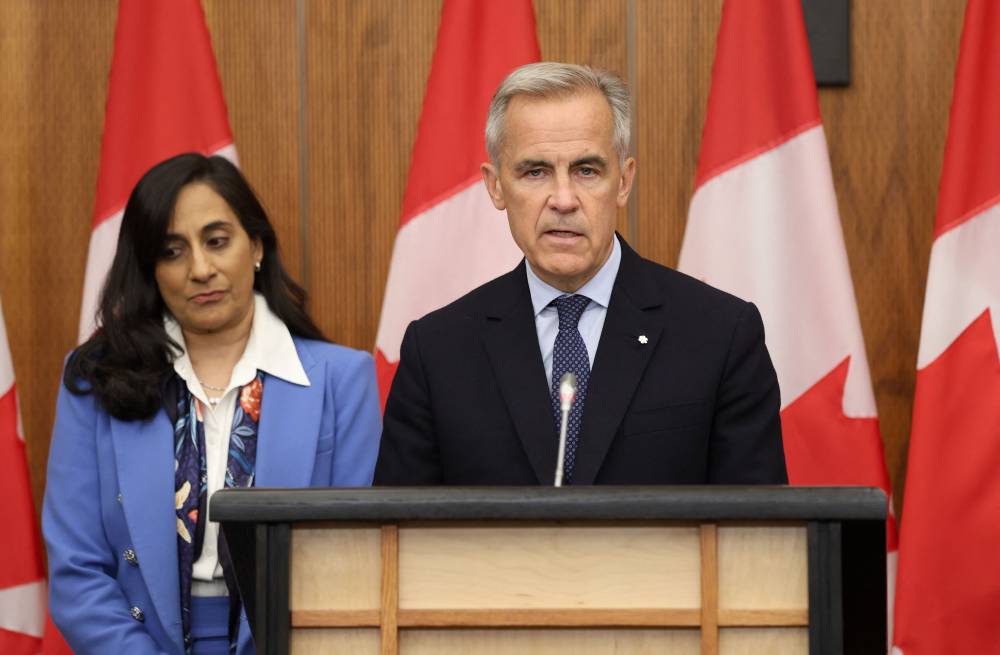 Canadian Foreign Affairs Minister Anita Anand listens to Canadian Prime Minister Mark Carney speak during a press conference after a Cabinet meeting to discuss both trade negotiations with the US and the situation in the Middle East, at the National Press Theatre in Ottawa, Ontario, Canada on July 30, 2025. (Photo by Dave CHAN / AFP)