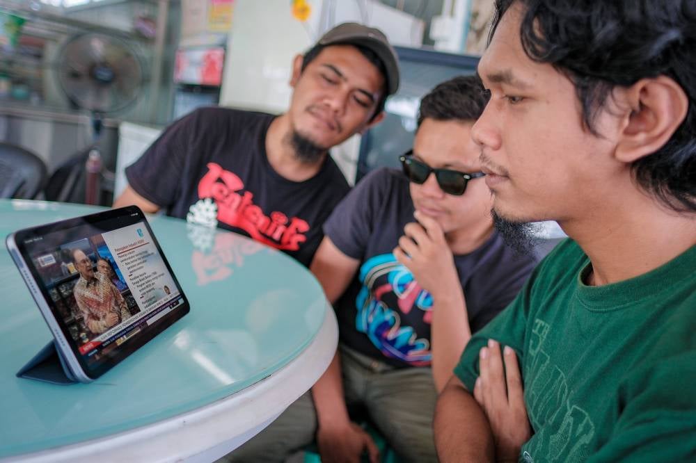 Youth Muhammad Ridhwan Abdul Fattah, 21, (right) and his friend watch the live online broadcast of the 13th Malaysia Plan (13MP) presentation by Prime Minister Datuk Seri Anwar Ibrahim, in Pekan Nanas, Pontian, today. Photo by Bernama