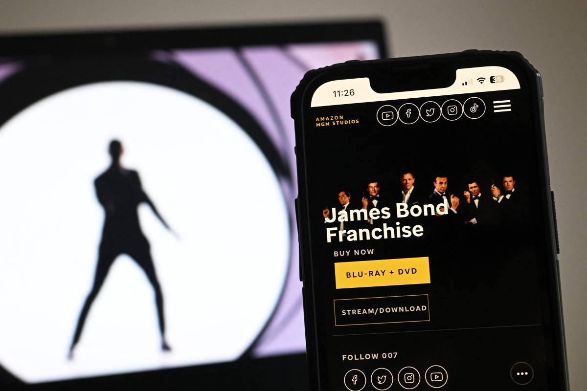 In this photo illustration created in London on February 23, 2025 the MGM Studios website displays James Bond Franchise details on a phone screen next to an photograph displayed on a laptop screen. James Bond in the hands of an American company: shock horror! Amazon's takeover of Britain's iconic Bond franchise has Her Majesty's subjects worried, with some wondering whether 007 still has a future. After months of wrangling between the films' producers and Amazon MGM studio, extensively reported in the British press, the final blow fell on Thursday, February 23: the American giant will now preside over the destiny of the world's best-known spy. (Photo by Justin TALLIS / AFP)