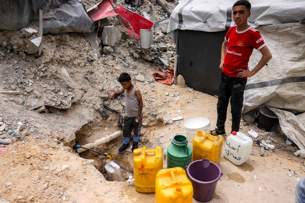 A boy fills up containers with water from the remaining water still left in underground pipes, in Beit Lahia in the northern Gaza Strip on April 24, 2025. - (Photo by BASHAR TALEB / AFP)