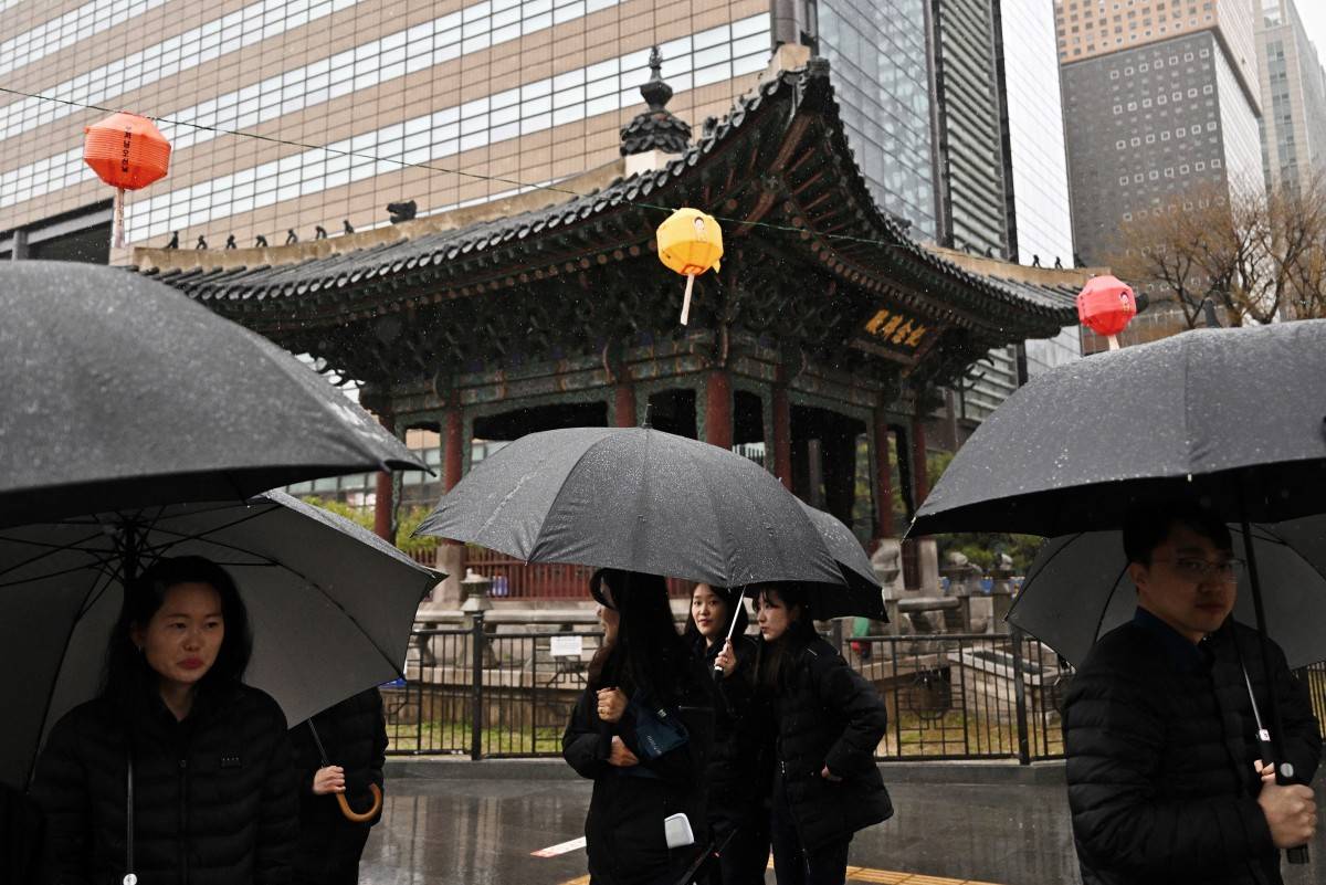 People hold umbrellas during light rain as they walk past a pagoda on a street in Seoul on April 5, 2025. - (Photo by PEDRO PARDO / AFP)