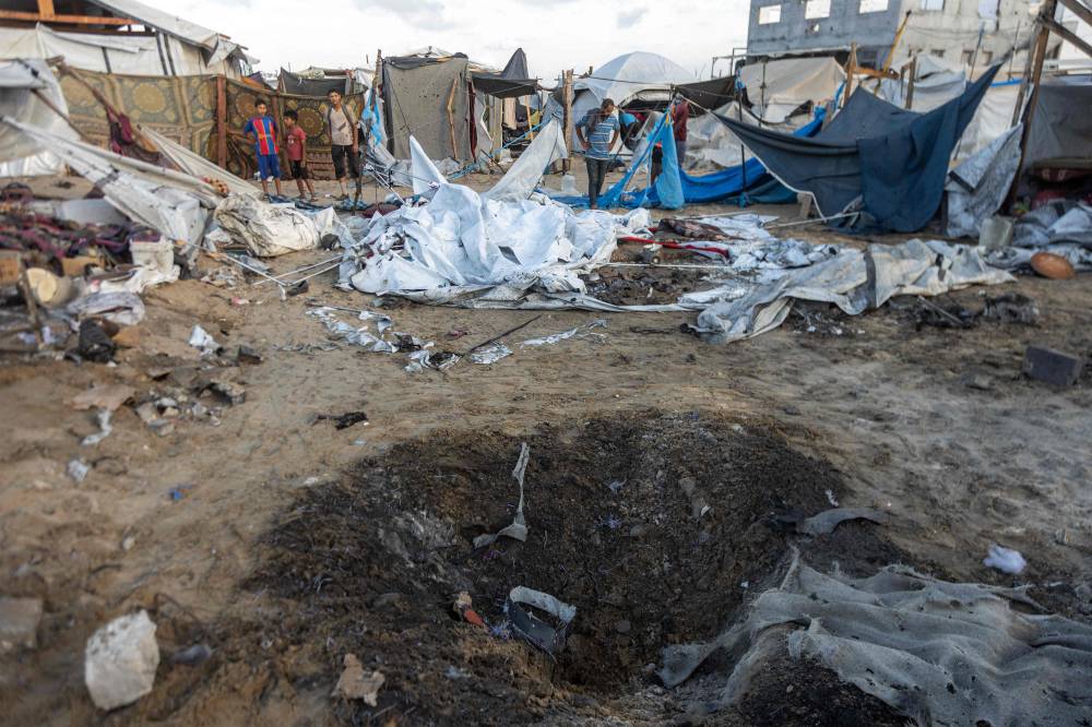 Boys stand by debris near a crater left by an explosion in the aftermath of overnight Israeli bombardment on a camp sheltering displaced people in the Mawasi area of Khan Yunis in the southern Gaza Strip on Aug 5. Photo by AFP