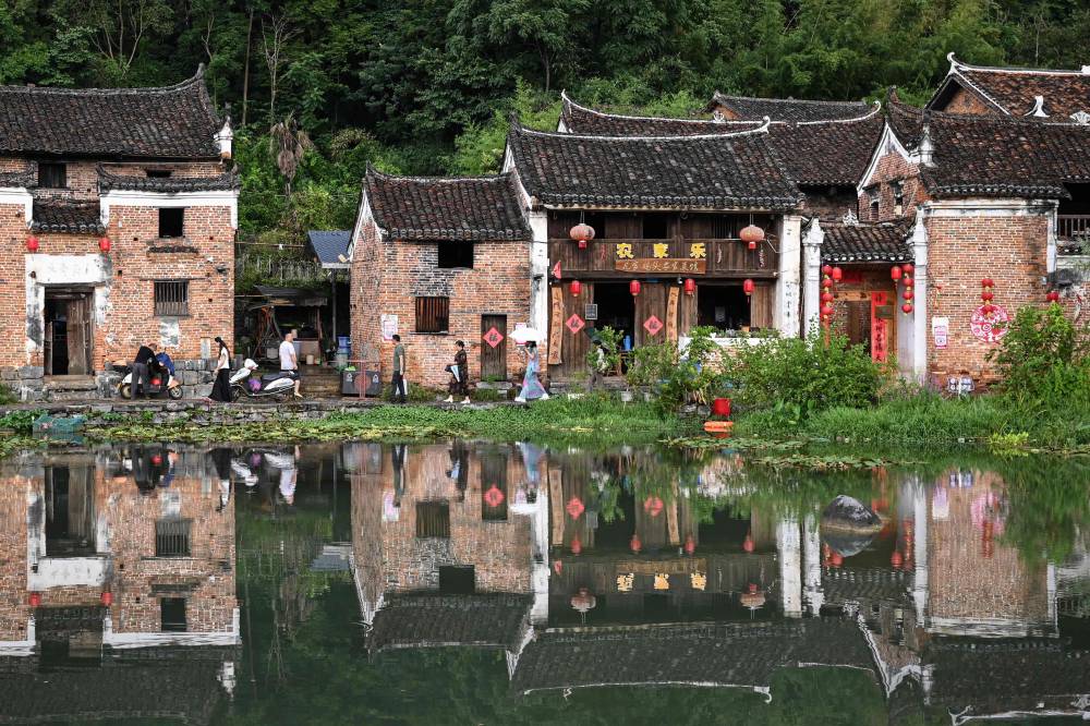The photo taken on July 21, 2025 shows Nushu inheritor He Yuejuan (C) walking on a street at Goulan Yao Village in Jiangyong county, southern China's Hunan province. Nushu, "female script", was created around 400 years ago when women were still barred from attending school. They secretly learned Chinese characters and adapted them into Nushu, using the script to communicate with each other through letters, songs, and embroidery. (Photo by Jade GAO / AFP)