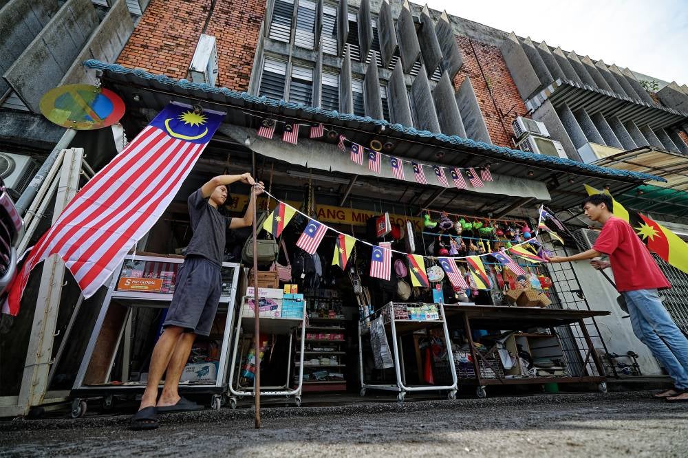 Two shop assistants put up the Sarawak state flag (Ibu Pertiwi) and the Jalur Gemilang in front of Guang Ming Bookstore at Kenyalang Park in conjunction with the National Month celebration. Photo by Bernama
