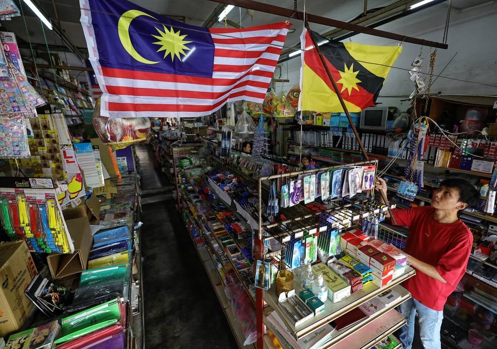 Shop assistant Fan Soon Hui, 31, puts up the Sarawak state flag (Ibu Pertiwi) and the Jalur Gemilang inside Guang Ming Bookstore at Kenyalang Park in conjunction with the National Month celebration. Photo by Bernama