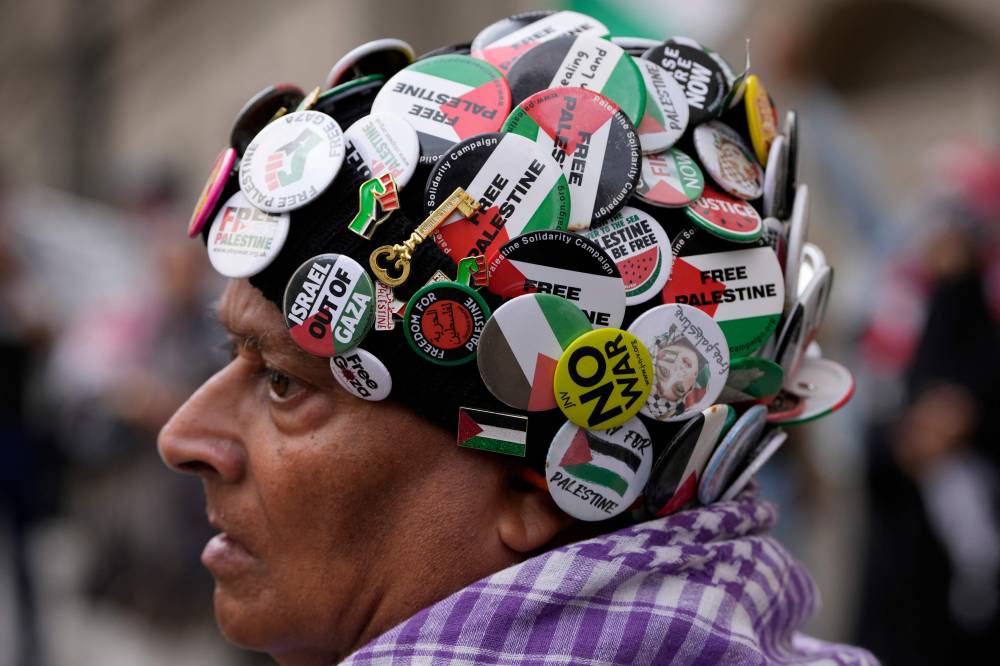 A supporter of five protesters appearing in court charged with aggravated burglary, criminal damage and violent disorder after a protest by the proscribed group Palestine Action at Israeli-linked firm Elbit, wears pro-Palestinian badges on a hat outside The Old Bailey in central London on August 22, 2025. (Photo by CARLOS JASSO / AFP)