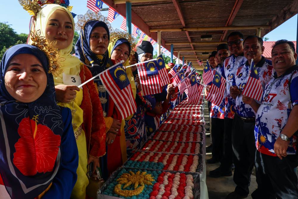 Kesedar Perkilangan Sdn Bhd chairman Mohd Syahbuddin Hashim and servers from the Parent-Teacher Association posing with the Jalur Gemilang made from onde-onde balls during the “Cetusan Jiwa, Semarak Merdeka” programme at the Kesedar Chalil Land Development Scheme (RKT), Gua Musang, today. - Photo by Bernama