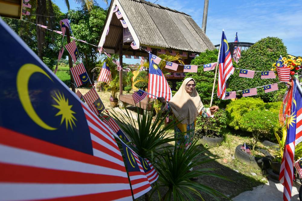Tuan Yah waving a Jalur Gemilang among the flags that adorn the area around her home in Kampung Kubang Bongor, Melor. She carries on her late husband’s tradition of flag raising. - Bernama photo