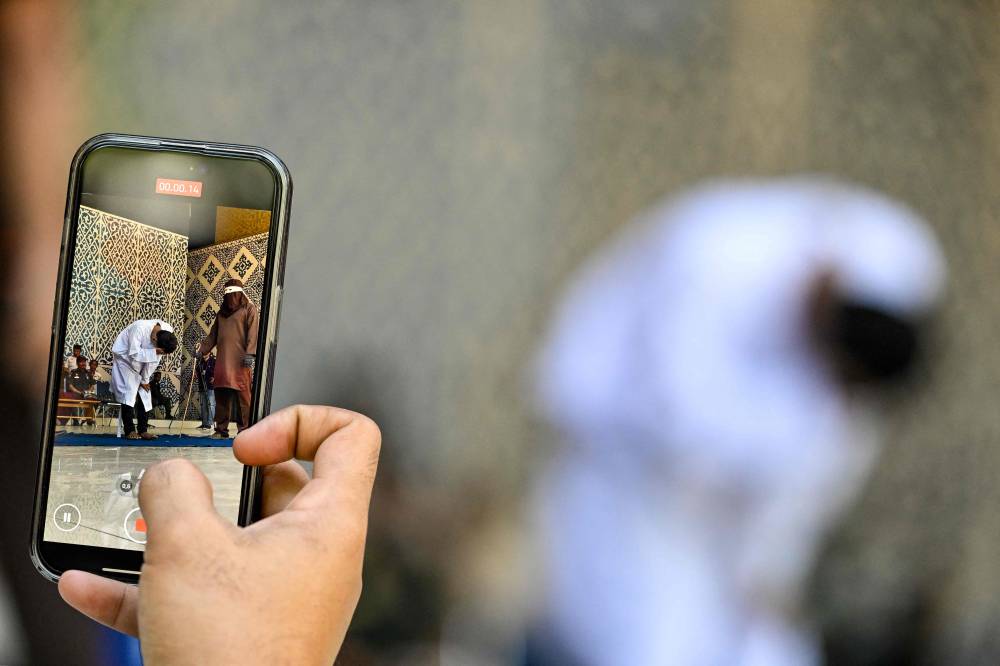 A man uses his mobile phone to shoot a video of a man accused of having gay sex as he gets publicly caned by a member of the Sharia police in Banda Aceh on Aug 26, 2025. - (Photo by CHAIDEER MAHYUDDIN / AFP)