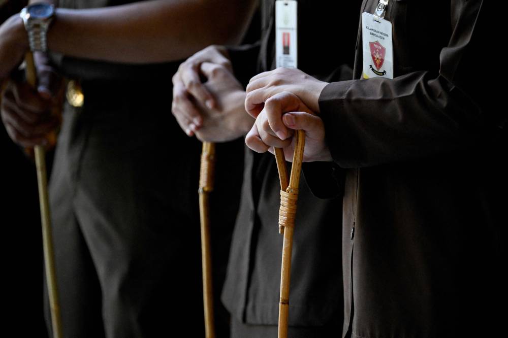 Law enforcement officers hold rattan sticks as a man accused of having gay sex waits to be publicly caned in Banda Aceh on Aug 26, 2025. - (Photo by CHAIDEER MAHYUDDIN / AFP)