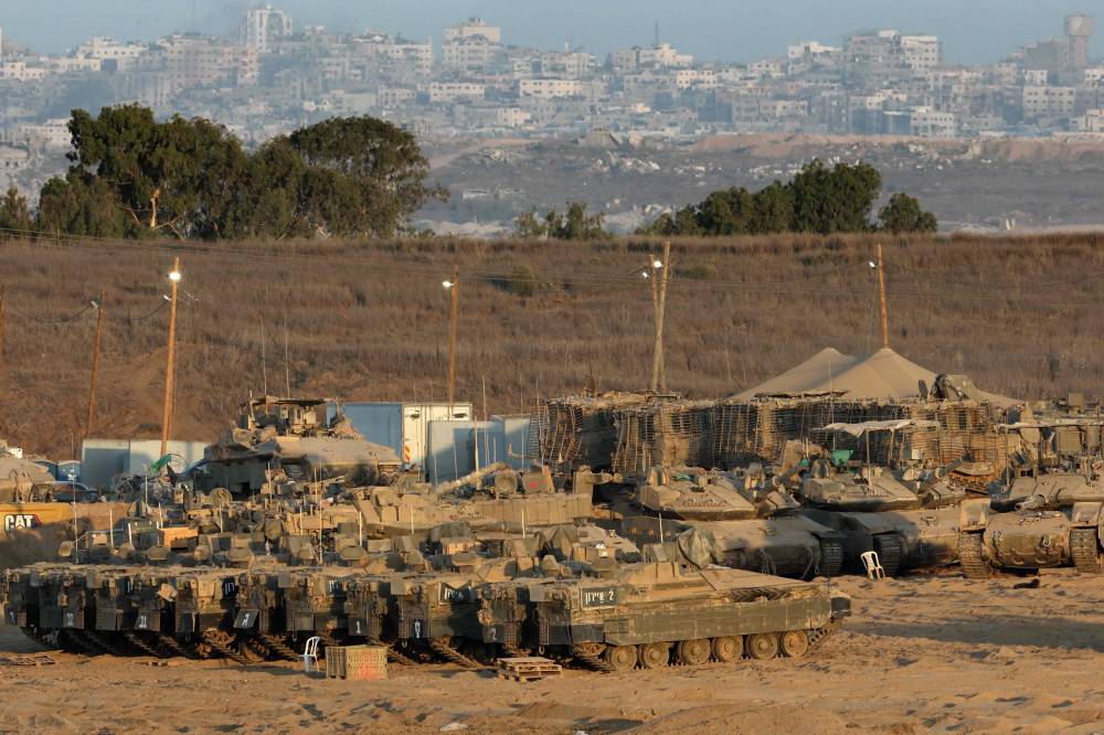 Israeli army vehicles are positioned in southern Israel on the border with the Gaza Strip (background) on Aug 29. Photo by Jack Guez/AFP