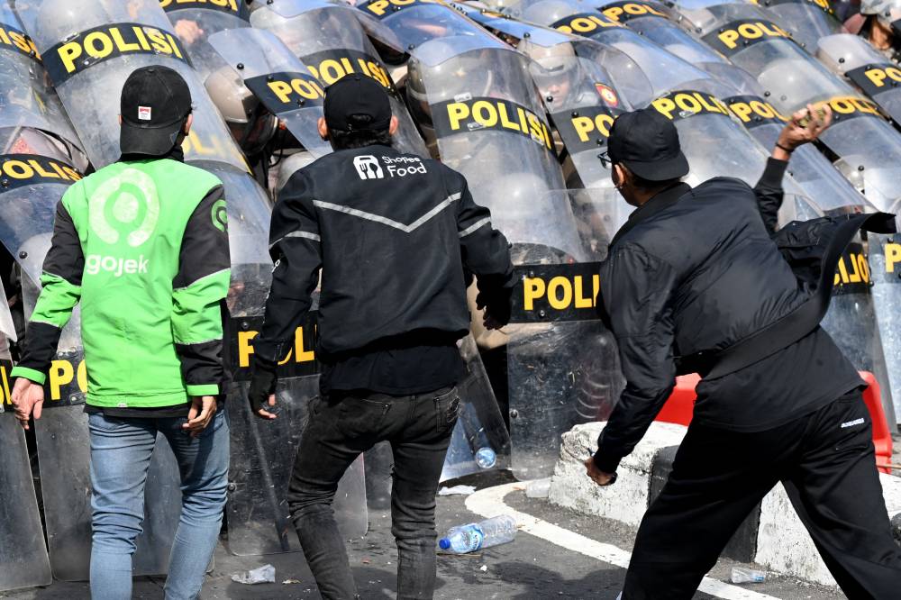 Protesters charge against police as the latter hold positions behind their shields during a demonstration in front of the Bali police station in Denpasar. Photo by AFP