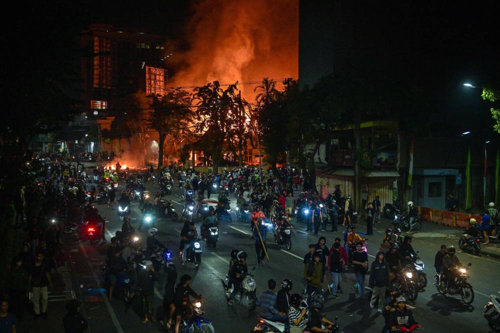 Protesters rides motorcycles in front of a police headquarters that was burned and looted during demonstrations in Surabaya on Aug 31, 2025. - (Photo by JUNI KRISWANTO / AFP)