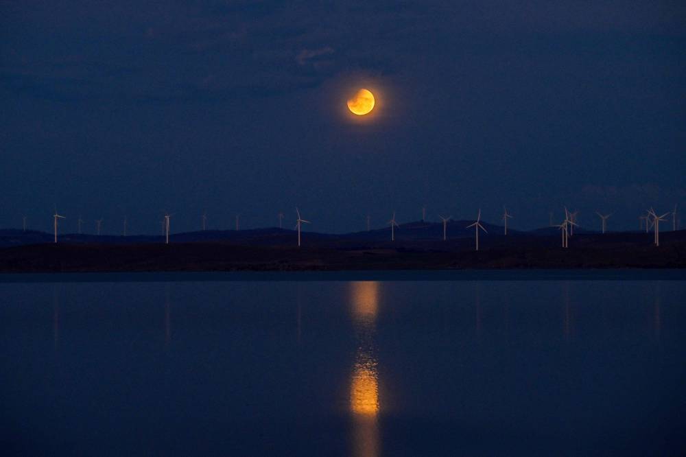A full moon, also known as the "Blood Moon," is seen during a partial eclipse in the sky over Lake George near the Australian capital city of Canberra on March 14, 2025. - (Photo by IZHAR KHAN / AFP)