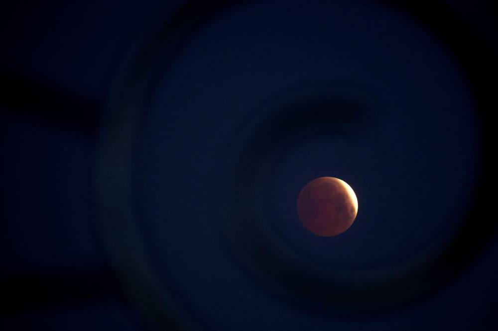 A rare 'blood Moon' total lunar eclipse is captured near totality from the village of Donon, 40 km from Pontevedra, in northwestern Spain, early on March 14, 2025. - (Photo by MIGUEL RIOPA / AFP)