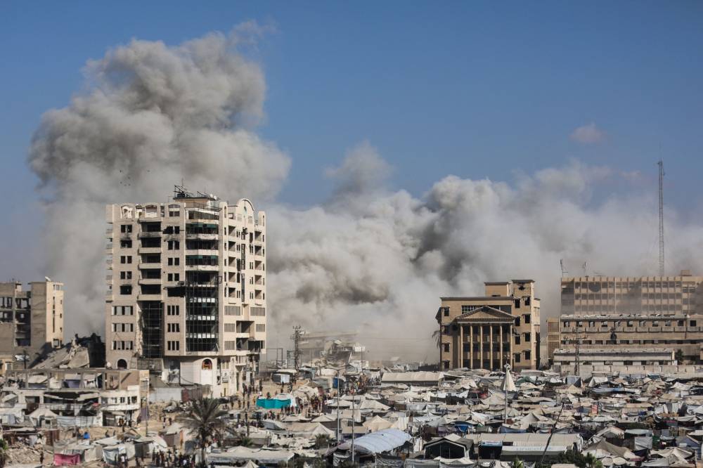 Smoke billows near tents sheltering displaced Palestinians after Israeli bombardment destroyed a building called al-Ruya Tower, in Gaza City's Rimal area, on Sept 8, following Israel's announcement that it would target tall buildings identified as being used by Hamas ahead of its forces' planned conquest of the urban hub. Photo by Omar Al-Qattaa/AFP