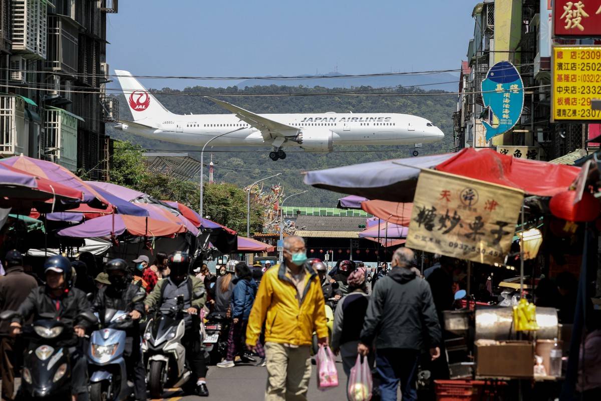 A Japan Airlines passenger plane lands as people visit a market in Taipei on March 20, 2025. (Photo by I-Hwa Cheng / AFP)
