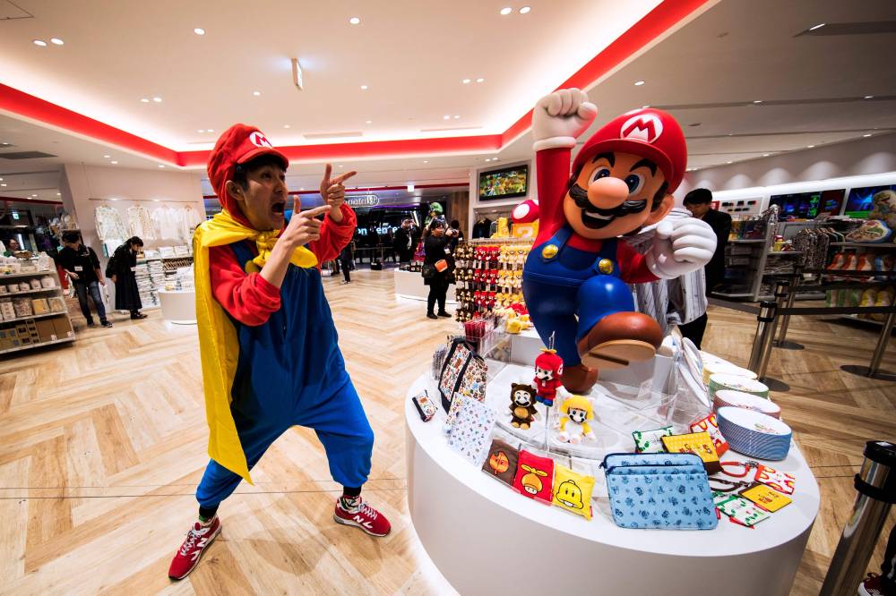 (FILES) This file photo taken on November 19, 2019 shows a man wearing a costume of Nintendo game character Mario posing next to merchandise displayed at a new Nintendo store during a press preview in Tokyo. Over four decades Nintendo's mascot
