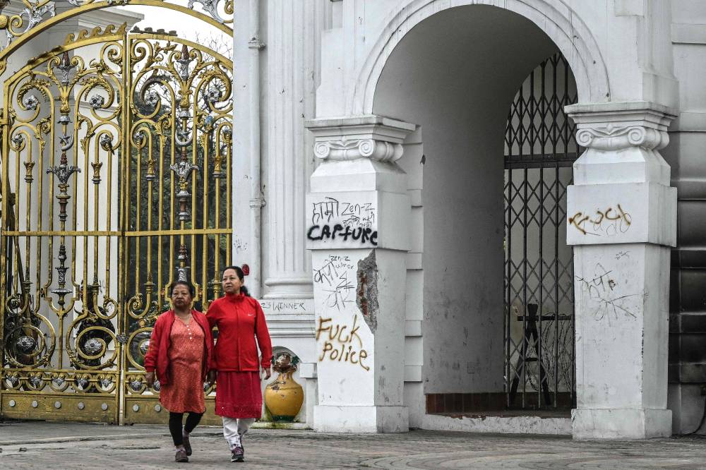 People walk past Singha Durbar, the main administrative building for the Nepal government, after it was set ablaze by protesters, in Kathmandu on Sept 12, 2025, during relaxation hours amid a curfew imposed to restore law and order. - (Photo by ARUN SANKAR / AFP)
