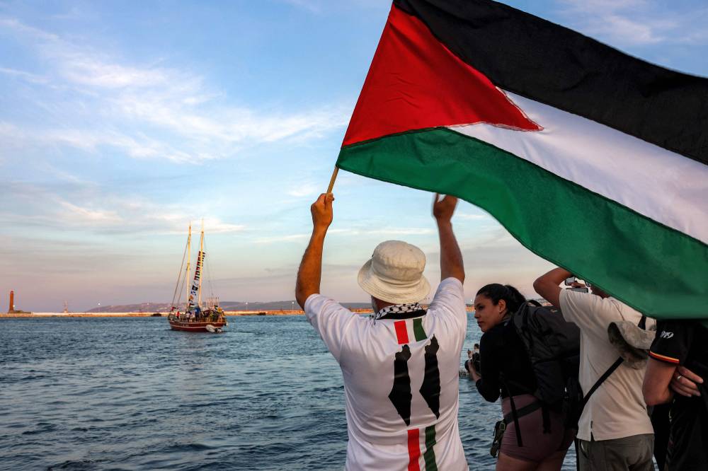 A man waves a Palestinian flags to other activists and human rights defenders riding aboard a vessel departing from Tunisia's northern port of Bizerte on Sept 14, 2025 to join the last boats taking part in the Global Sumud Flotilla, bound for the Gaza Strip to break Israel's blockade on the Palestinian territory. - (Photo by MOHAMED FLISS / AFP)