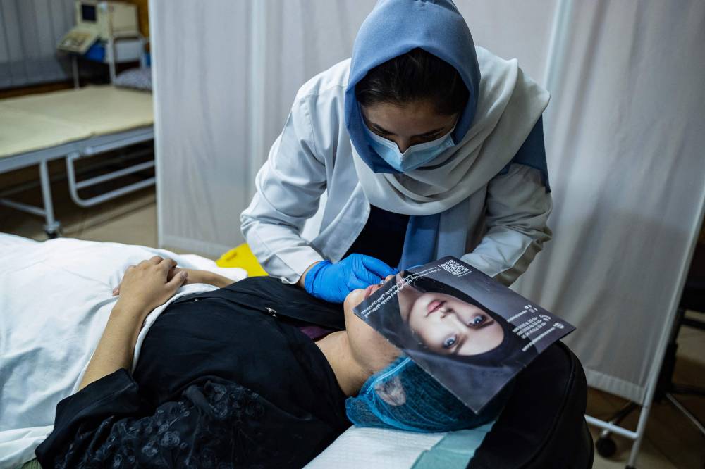 In this photograph taken on August 13, 2025, a member of the medical staff injects fillers into an Afghan women's lips at a beauty clinic in Kabul. Decked with fake crystal chandeliers and velvet sofas, cosmetic surgery clinics in Afghanistan's capital are a world away from the austerity of Taliban rule, where Botox, lip filler and hair transplants reign. (Photo by Wakil KOHSAR/AFP)