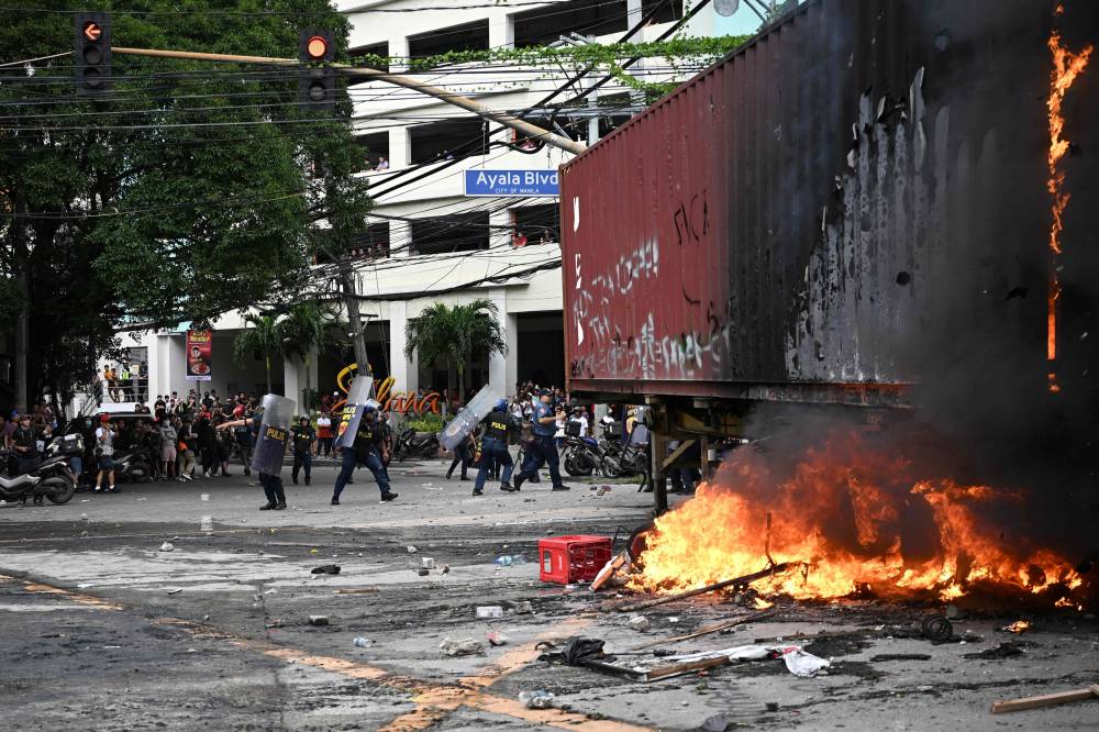 Policemen shield themselves from rocks thrown by protesters after setting fire to a trailer van near Malacanang Palace in Manila. Photo by Ted Aljibe/AFP