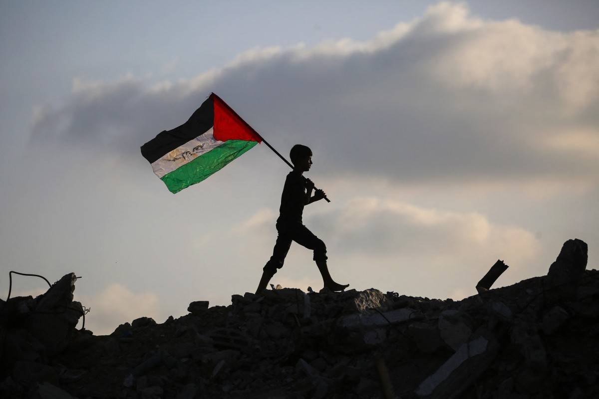 A displaced Palestinian child waves a Palestinian flag as he walks on the rubble of a destroyed building at the Bureij camp for refugees in the central Gaza Strip on Sept 22, 2025. - (Photo by EYAD BABA / AFP)